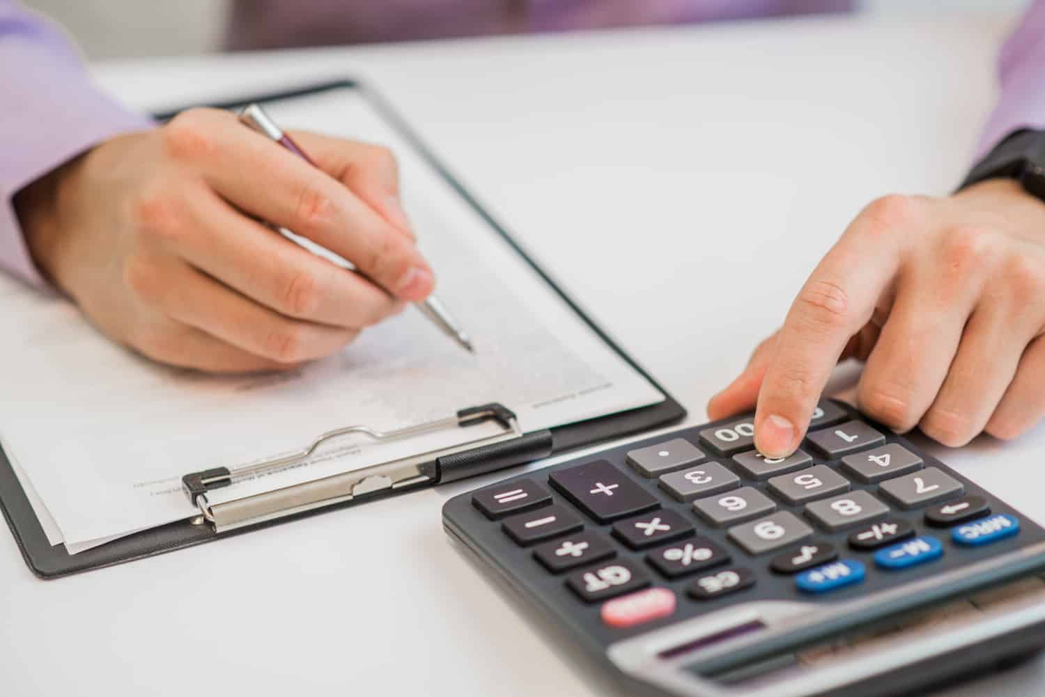Uma mão usando uma calculadora e fazendo anotações em uma folha de papel