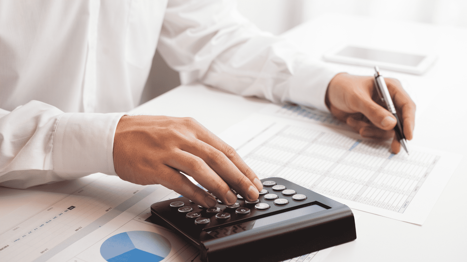Um homem com uma calculadora, fazendo anotação em uma planilha de papel