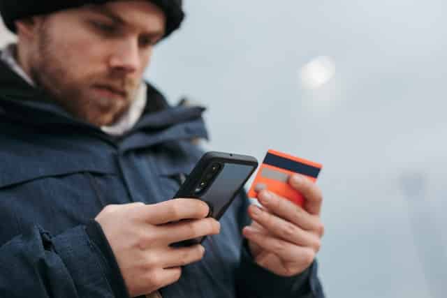 Homem segurando cartão de crédito e celular