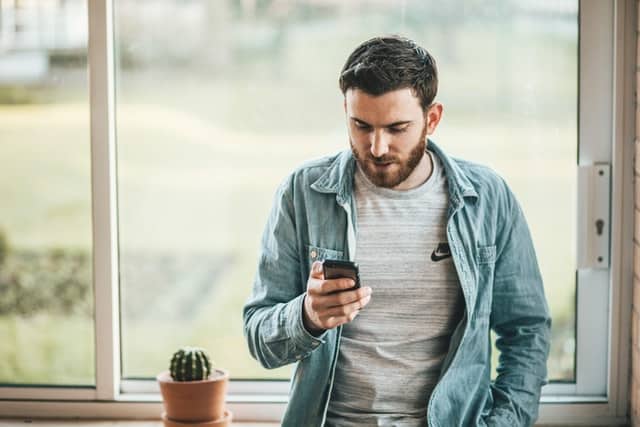 Homem encostado na janela segurando um celular para representar o design responsivo