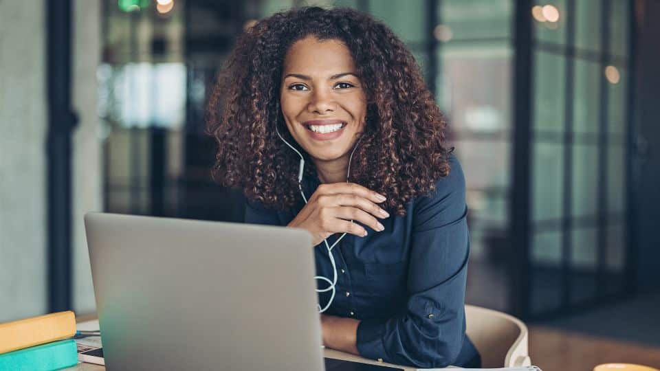 Mulher sorrindo com fone de ouvido e notebook em sua frente.